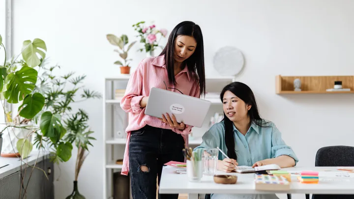 Une femme montre l'écran de son ordinateur portable à une collègue assise à son bureau